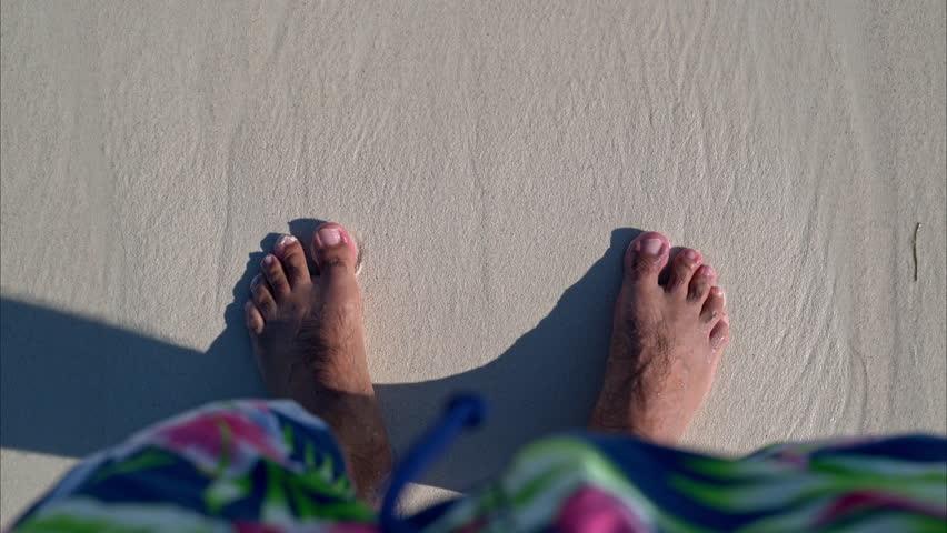 Slow motion POV of a suntanned man standing on the sand at a caribbean beach getting washed by the waves in Cancun Mexico