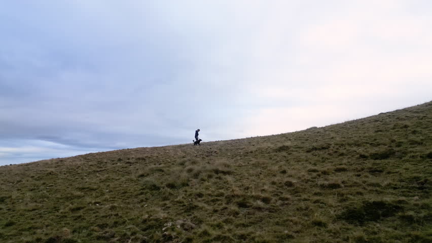 Drone shot of a woman and her dog walking on the top of a mountain range