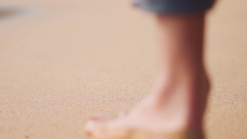 Closeup shot of footprint on the sand of the Kakolem beach with defocused man walking in background at Goa, India. Selective focus on the footprint left behind by the man walking barefoot on the beach
