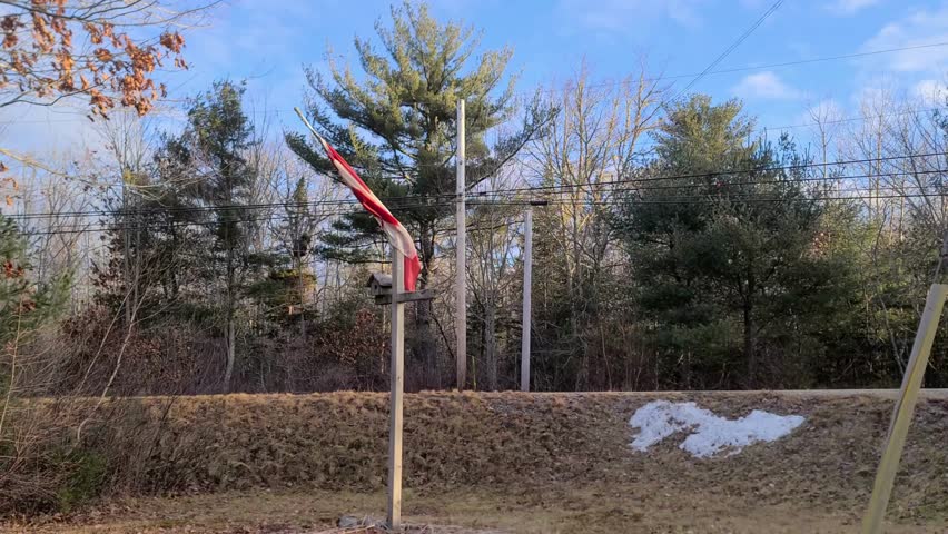 A Canadian flag curled up and attached to a post, which is barely blowing in the wind.