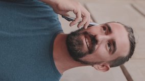 VERTICAL VIDEO, Close-up of young man with beard talking on cellphone against the background of the old city