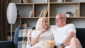Smiling senior couple watching TV and eating popcorn while sitting on sofa at home and hugging. - Powered by Shutterstock - Get 15% off with code: PIKWIZARD15