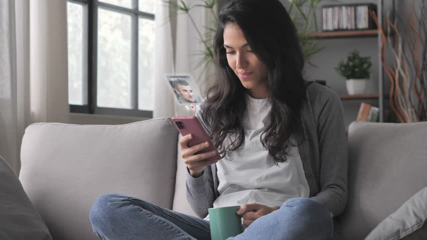 young woman using smartphone augmented reality dating app,brunette female sits on couch uses smart phone browsing men profiles flirting on social media application searching for love Royalty-Free Stock Footage #1100018807