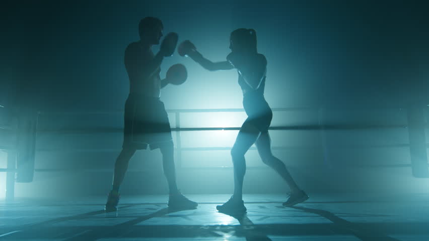 Close-up shot of a man training a woman at the gym. Unrecognized coach working out with female kickboxer indoors. High quality 4k footage in cold teal blue foggy back light | Shutterstock HD Video #1100019003