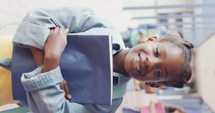 Vertical video of portrait of happy african american schoolgirl in school. Education, inclusivity, school and learning concept.
