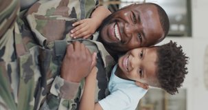 Vertical video of portrait of african american male soldier and his son embracing. Spending quality time at home.