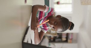 Vertical video of thoughtful african american girl using laptop in online lesson, copy space. Childhood, education, learning, communication and domestic life.
