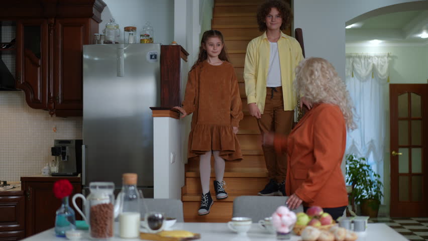 Happy children walking downstairs hugging woman smiling. Loving Caucasian mother greeting son and daughter at breakfast table in the morning talking. Family lifestyle | Shutterstock HD Video #1100022031