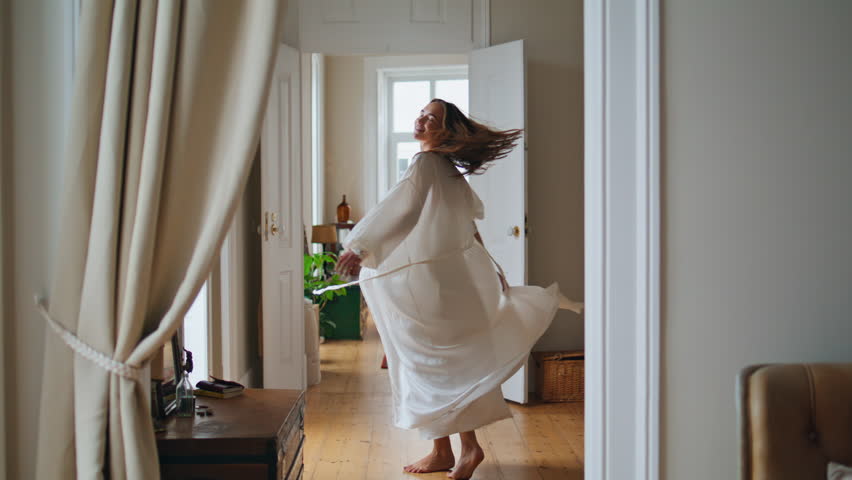 Dancing lady moving slowly at beige apartment. Lazy girl feeling joyful at light room. Happy woman in pyjamas enjoying weekends start at cozy home. Lovely female person welcoming new day alone at hall | Shutterstock HD Video #1100022215