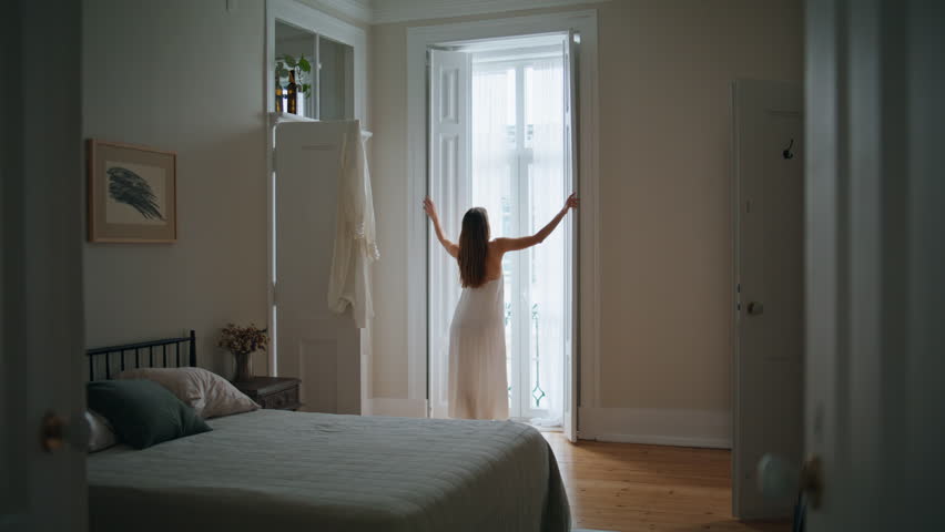 Young woman opening blinds at home morning. Relaxed girl looking window greeting new day back view. Unknown lady in silk robe enjoying weekend alone at light apartment. Domestic lifestyle concept | Shutterstock HD Video #1100022355