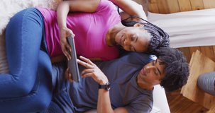 Vertical video of african american couple sitting on sofa and using tablet in log cabin. Free time and domestic life concept.