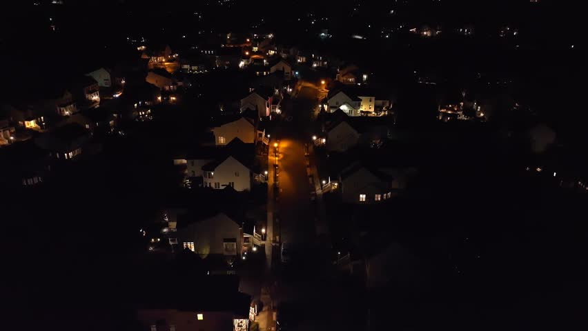 Lights illuminate large houses in upscale neighborhood in America at night. Aerial dolly forward shot of homes in development at dark.