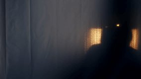 Silhouette of a man in a hood with glowing eyes behind a transparent curtain, pulling his hand into the camera. The concept of demons, paranormality, ghosts. 4k slowmo video with speed ramp effect.
