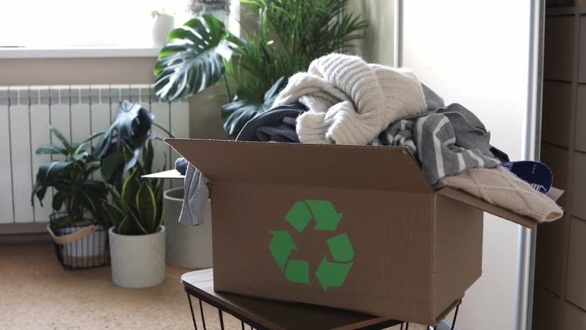 Clothing recycling concept. Old clothes fall into a box with a recycling sign in the home room near the wardrobe. Decluttering and minimalism. Spring cleaning. | Shutterstock HD Video #1100030043
