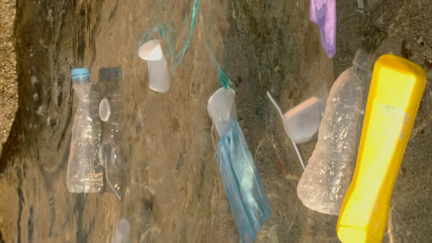 Vertical video, Close-up of disposable plastic, face mask and other debris swim on the water in surf zone. Plastic and other garbage on the seashore. Slow motion | Shutterstock HD Video #1100031737