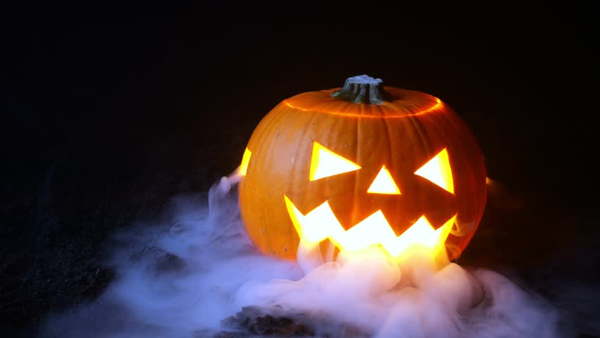 Smoke coiled from the face of a Halloween Pumpkin with different colored lights. | Shutterstock HD Video #1100032981