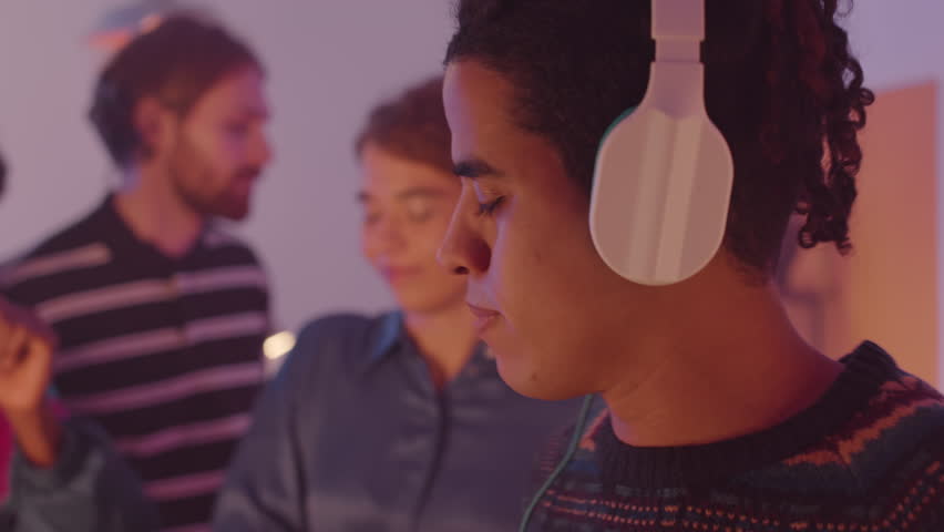 Tilt down shot of Biracial guy in headphones listening to music on cassette player and dancing while having 80s house party with friends