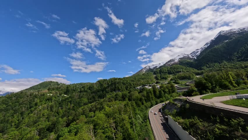Aerial view white sports car speed riding on serpentine asphalt road summer mountain landscape alpine sunny resort. FPV drone flying over fast automobile under bridge surrounded by nature scenery 4k Royalty-Free Stock Footage #1100035589