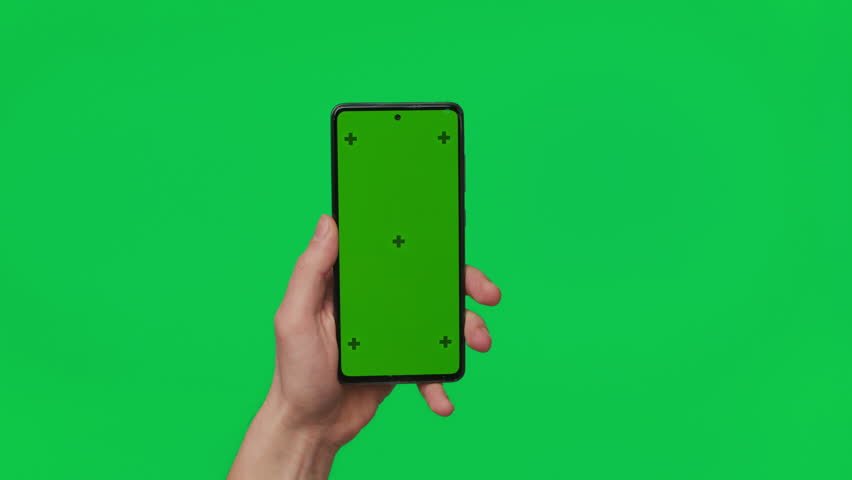 Male hand holding a smartphone with vertical green chroma key screen isolated on green. Mobile phone in a hand. Different signs and gestures with fingers. The concept of technology and internet. Royalty-Free Stock Footage #1100036441