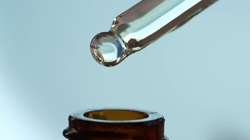 Glass dropper macro with falling drops of oil, serum, peptide into a brown cosmetic bottle. Royalty-Free Stock Footage #1100036499