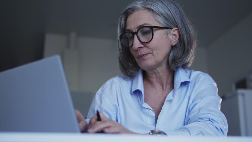 Adult gray-haired woman applicant typing her curriculum vitae, seeking for a job