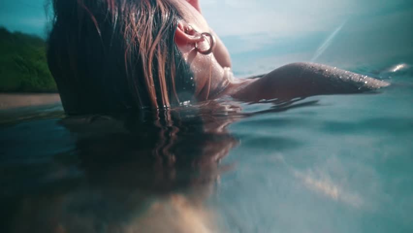 An Asian woman floating on the seawater while swimming on the beach on an island during the day | Shutterstock HD Video #1100038353