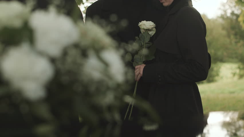 Cropped shot of unrecognizable woman in black coat holding two white roses in hands at outdoor funeral ceremony Royalty-Free Stock Footage #1100039531