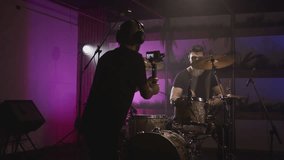 Shooting a music video. The director of photography makes a video, shoots a drummer musician. The view behind the scenes. Create a music video for a rock band. Creative director and crew.