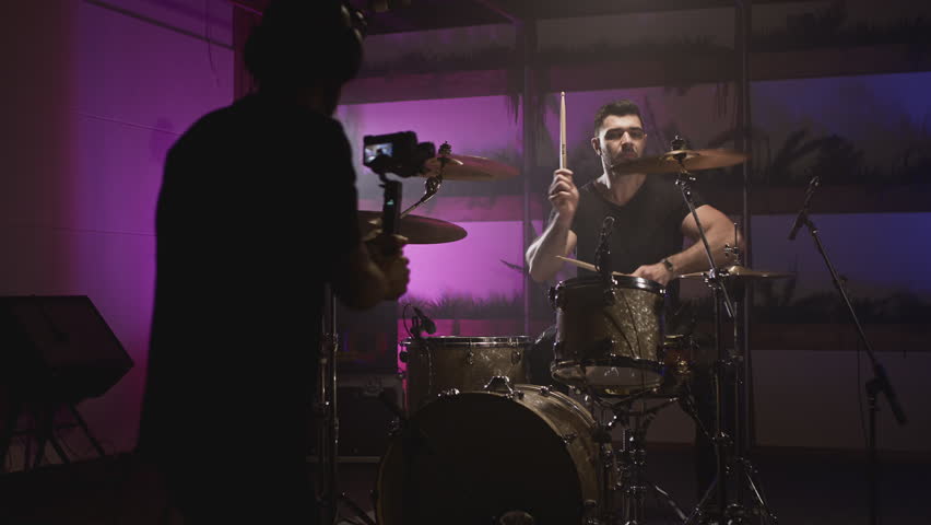 Shooting a music video. The director of photography makes a video, shoots a drummer musician. The view behind the scenes. Create a music video for a rock band. Creative director and crew. | Shutterstock HD Video #1100041771