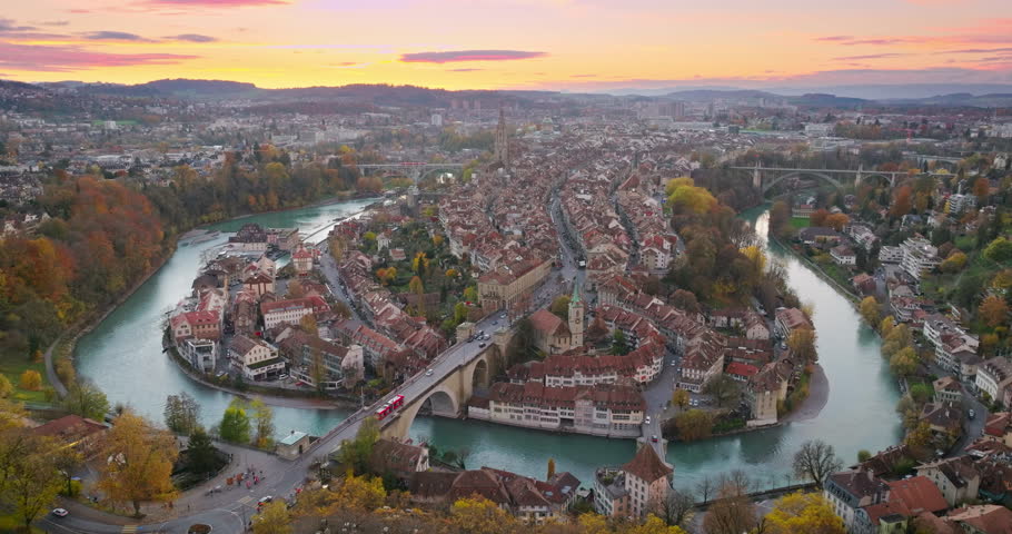 Wide establishing aerial pink sunset. Bern town, the capital city of Switzerland with colorful twilight romantic sky. Drone fly over Aare river Swiss historic cityscape traveling landmark in autumn.