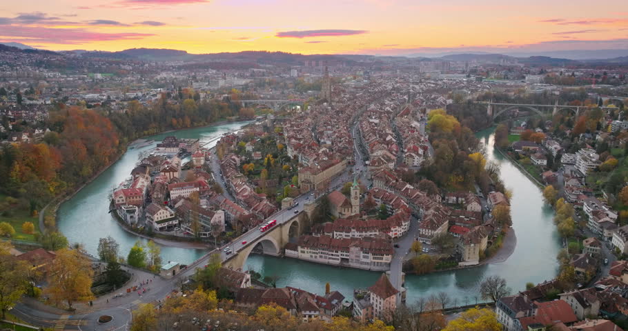 Wide establishing aerial sunset over Bern town, the capital city of Switzerland with colorful twilight romantic sky. Drone fly over Aare river Swiss historic cityscape traveling landmark in autumn.
