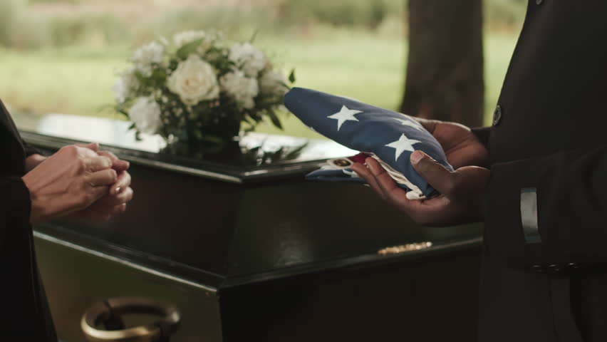 Cropped shot of unrecognizable military chaplain presenting US burial flag to widow of deceased veteran during outdoor funeral ceremony