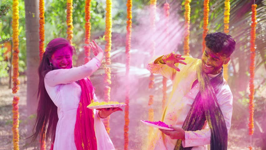 Happy excited couple playing holi together at festival ceremony - concept of playful or fun, togetherness and colourful Indian tradition