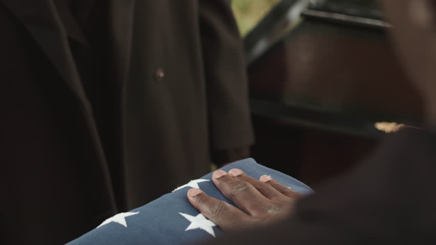 Closeup of unrecognizable African American military chaplain giving folded US burial flag to widow of deceased soldier at funerals