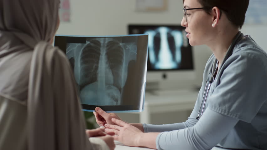 Confident female radiologist showing result of medical examination to patient in hijab while sitting in front of her during presentation and description of x-ray details and consultation | Shutterstock HD Video #1100044007