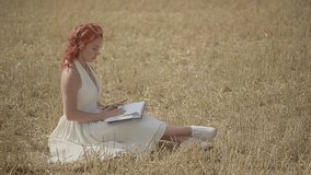 the girl is sitting on the lawn leafing through the pages of a book in a wheat field. High quality Full HD video recording. slow motion video
