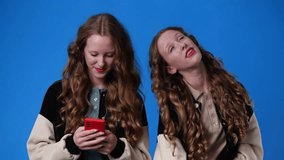 4k video of twin girls using their phones on blue background.