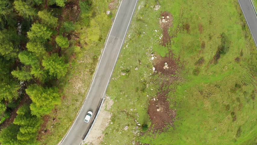 Driving car travels on famous sightseeing Snake Road on Giau Pass. White vehicle turns on asphalt roadway serpentine curve on hill slope