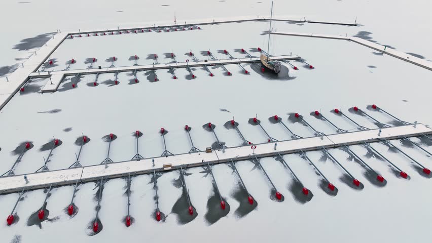 Aerial View of dead frozen harbour docks with boat and ice below. Extreme cold weather. Nature landscape famous for being heavily affected by global warming and Climate Change. Mooring for yachts
