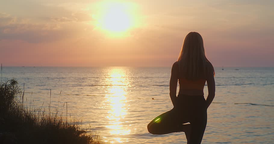 Young women are doing yoga in summer sunset with sea background. Warm-up, healthy life, relaxing and outdoor exercise. Health care, authenticity, sense of balance and calmness. | Shutterstock HD Video #1100057791
