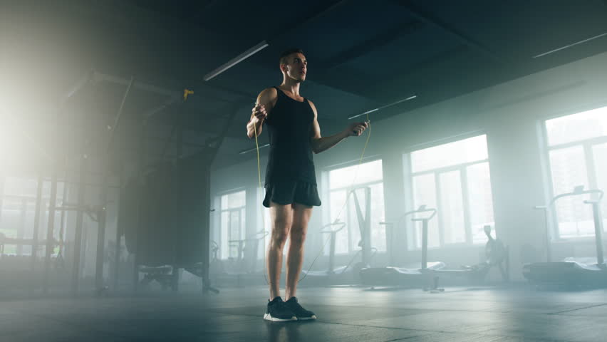 Close-up view of active man using a jumping rope to improve muscle strength. Portrait of a skilled sportsman enjoying challenging exercise routine in modern gym. High quality 4k footage Royalty-Free Stock Footage #1100058499