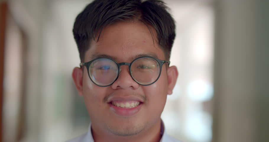 A little smile of an Asian male teenage high school student wearing thick glasses standing on the corridor in the building. | Shutterstock HD Video #1100063945