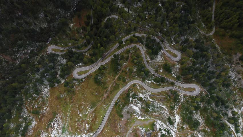 Rising aerial footage above a winding road, a lush green forest, and a crystal clear lake. 