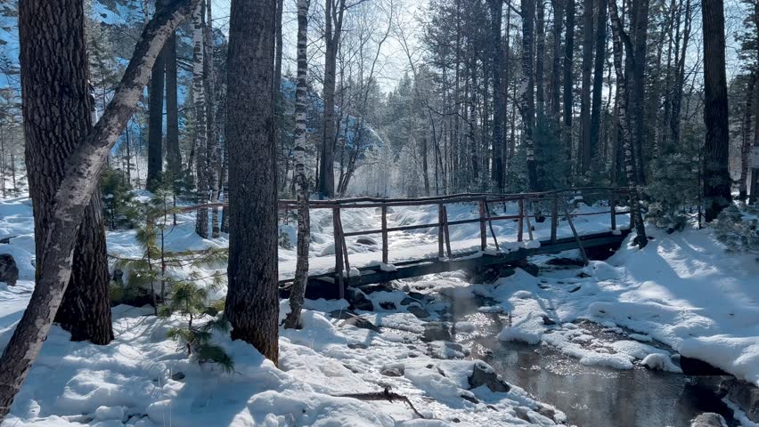 Winter landscape of a stream among a pine forest in a gorge among the snow-capped mountains Winter landscape of a suspension bridge across a frozen stream in the forest mountains Winter landscape 