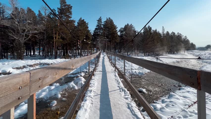 Winter landscape of a suspension bridge across a frozen stream in the forest mountains Winter landscape against the backdrop of the snow-capped mountains, Arshan, Siberia, Buryatia. High quality 4k fo