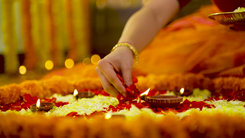 Close up shot of woman hands decorating Rangoli design with flowers for diwali festival celebration on floor at home with diya or lamps - concept of festival preparation, Indian culture and planning. Royalty-Free Stock Footage #1100079937