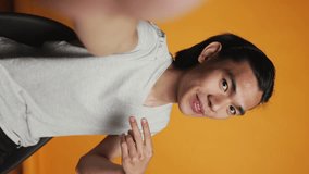 Vertical video: POV of asian smiling man taking pictures on camera, acting funny and silly over orange background. Cheerful casual model posing for photos in studio, smiling and being happy. Carefree