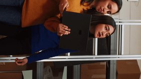 Vertical video: Team of asian women analyzing stock in boxes, working with distribution and order logistics in warehouse space. Young workers using laptop to check inventory, business management