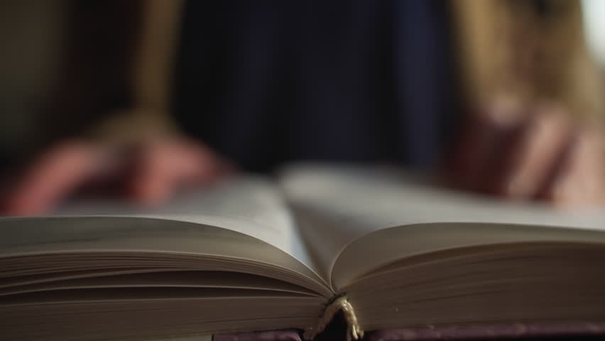 book reading. closeup side view book on table. man leafs through book page and reads the text following his finger. reading literature and education. shallow depth of field. cinematic DOF Royalty-Free Stock Footage #1100084015