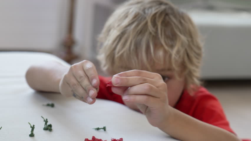 Close up child face playing with toy soldiers. One imaginative small boy plays with miniature combat figurines